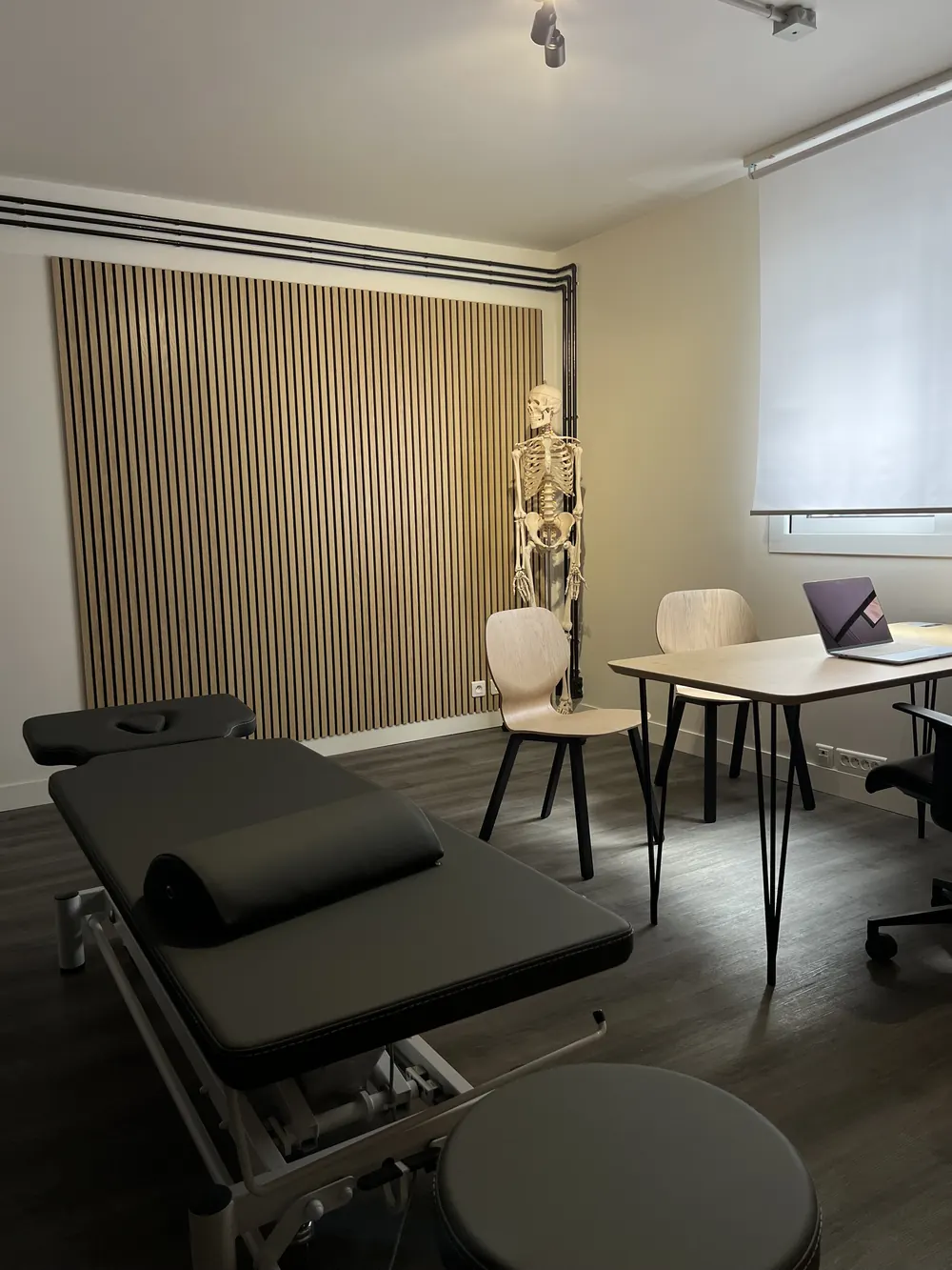 Espace de soin du cabinet d'ostéopathie : table de traitement, squelette anatomique et mur en tasseaux de bois